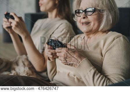 Happy Senior Mother And Adult Daughter Playing Video Game, Holding Remote Controllers, Enjoying Leis