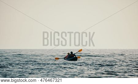 Happy Couple Kayaks In An Inflatable Kayak On The Sea At Sunset. Couple Kanoeing In The Sea Near The