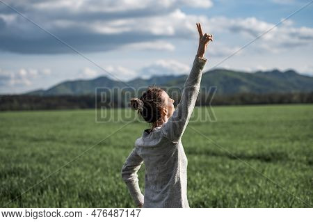 Authentic Young Woman Standing Under Dramatic Spring Sky With Her Arm Raised In Victorious Gesture. 