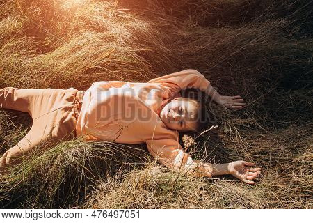 A Joyful Boy Lies In Tall Grass In A Meadow. Outdoor Leisure In The Park. Top View