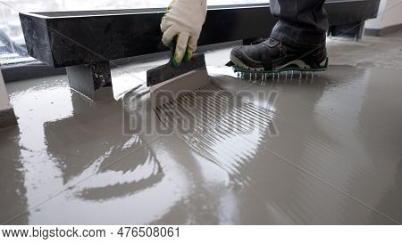 Repairman In Protective Gloves And Uniform Using Metal Spatula For Aligning Liquid Self-levelling Fl