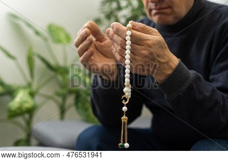 An Elderly Man Prays With A Rosary And The Flag Of The United Arab Emirates