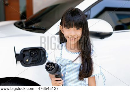 A Playful Girl Holding And Pointing An Ev Plug, A Home Charging Station Providing A Sustainable Powe
