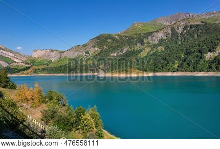 Lake Of Roselend And Blue Turquoise Water Borded By Mountains  In French Alps Under Blue Sky