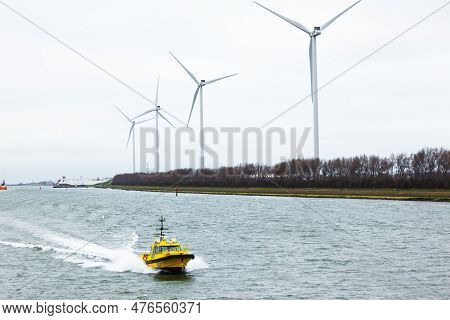 Wind Farms On The Shore Along A Water Canal In The Netherlands And A Pilot Boat Sailing Along The Ca
