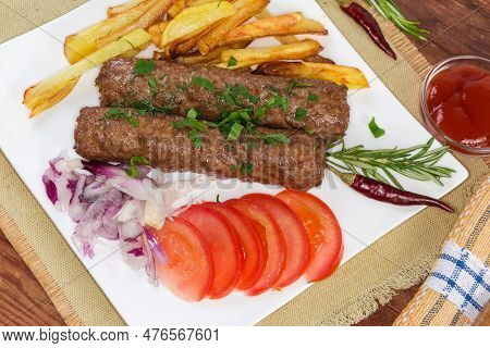 Serving Of The Two Baked Lula Kebab With French Fries, Chopped Vegetables And Sauce On The White Squ