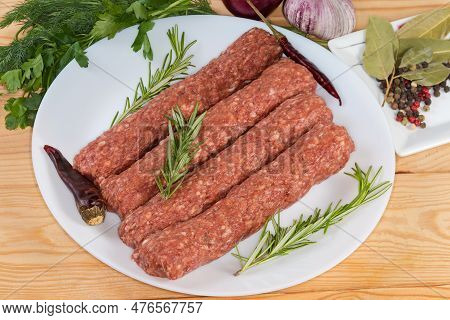 Several Raw Lula Kebab On Dish Among The Some Vegetables, Spices And Greens On The Rustic Table