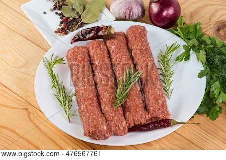 Several Raw Lula Kebab On Dish Among The Some Vegetables, Spices And Greens On The Rustic Table