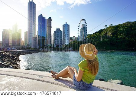 Holidays In Brazil. Attractive Young Woman Enjoying Sunset Sitting On Promenade In Balneario Cambori