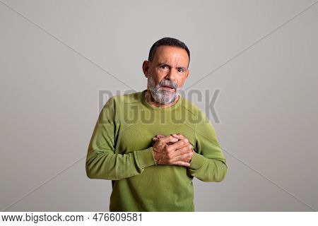 Unhappy Sad Caucasian Old Man In Casual Presses Hands To Chest, Suffer From Pain In Heart
