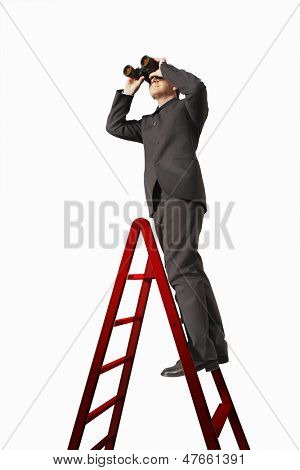 Full length of businessman on ladder looking through binoculars isolated on white background