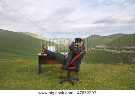 Vista laterale dell'uomo d'affari rilassanti con i piedi sulla scrivania in campo montagna