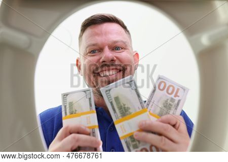 Smiling Man With Three-day Stubble Looks Into Toilet Bowl Holding Wads Of Dollars. Rich Male Looks F