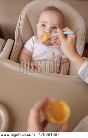 High Angle View Of Mother Feeding Cute Little Baby Boy With Porridge, Baby Sitting In High Chair All