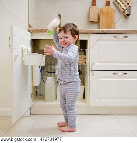 A Child Is Playing With Chemical Cleaning Products Under The Sink In The Kitchen. Baby Holds Bottles