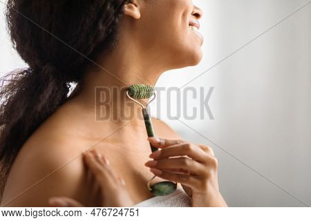 Anti-aging Skincare. Smiling Black Woman Massaging Neck Skin With Greenstone Jade Roller