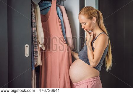 A Pregnant Woman Has Nothing To Wear. A Pregnant Woman Stands In Front Of A Closet With Clothes And 