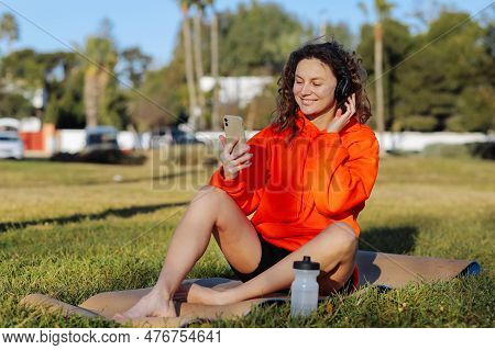 Young Smiling Sportswoman In Wirelles Headphones Listening Music And Using Cellphone During Workout 