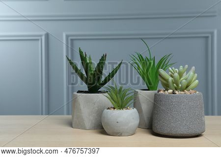 Many Different Artificial Plants In Flower Pots On Wooden Table Near Grey Wall, Space For Text