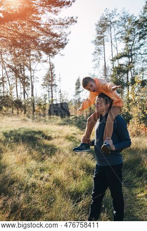 Dad And Son On A Walk In The Forest In Sunny Weather. Family Leisure. The Father Carries His Son On 