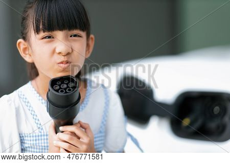 A Playful Girl Holding And Pointing An Ev Plug, A Home Charging Station Providing A Sustainable Powe