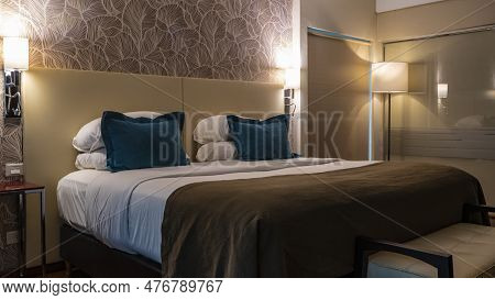 Bedroom Interior. The Double Bed Is Covered With A Blanket And A Bedspread. Pillows Are Stacked. The