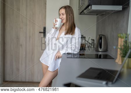 Beautiful Young Girl Is Standing In The Kitchen And Drinking Coffee. Morning Routine. Wearing White 