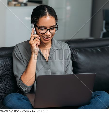 Young Female Entrepreneur In Thought Sitting On The Floor In The Kitchen With A Laptop On Her Legs