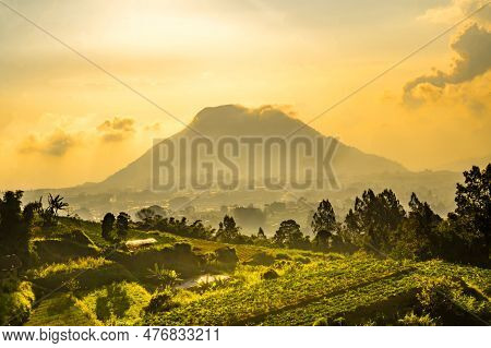 View Of Merbabu Mountain In Indonesia During Hazy Sunset With Green Village Foreground.