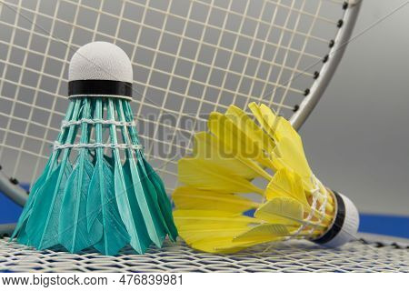 Feathered Shuttlecocks In Blue And Yellow Near Badminton Rackets Over Grey Background, Selective Foc