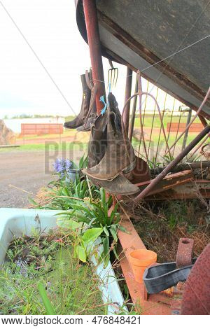 Old Brown Boots Hanging From A Rusted Pipe Outside A Horse Saddle. Unused Boots Hanging Outdoor. Sma