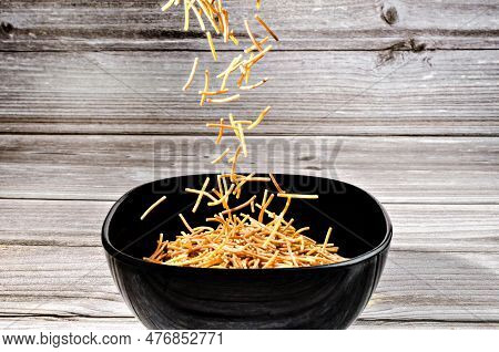 Close-up Of Cooked Polyphosphate Noodles Falling Into A Ceramic Bowl On A Wooden Table