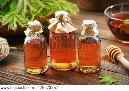 Three Bottles Of Maple Syrup Or Healthy Tincture And Spring Maple Leaf. Bowl Of Maple Syrup And Wood