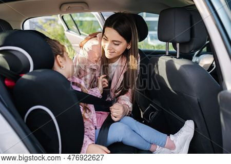 Attractive Young Mother Put Her Daughter In A Car Seat And Fastens Her Seat Belts. Woman Care About 