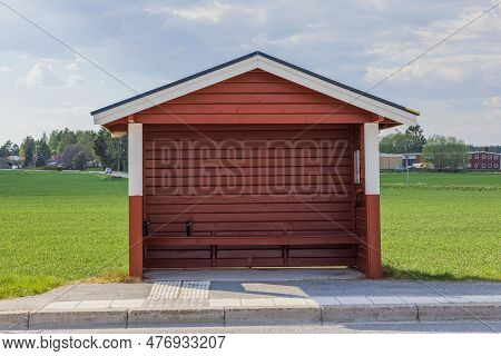 Close Up View Of Swedish Old Style Traditional Red Wooden Bus Stop On Green Field Background.
