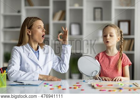 Speech Therapy Concept. Cute Little Girl Pronouncing Sound O Looking At Mirror