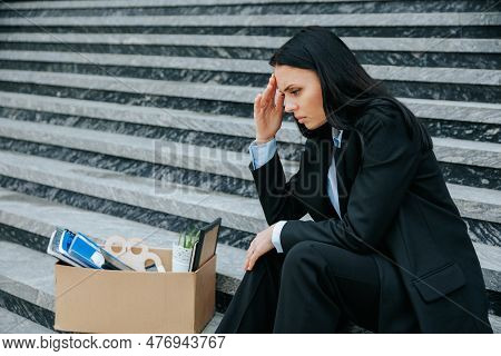 A Powerful Photo Of A Woman Sitting On Stairs, Holding A Cardboard Box, Representing The Physical An