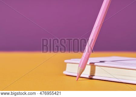 Pink Pencil Tip Touching Orange Desk On Magenta Lilac Background With Diary Or Copybook. Office Or S