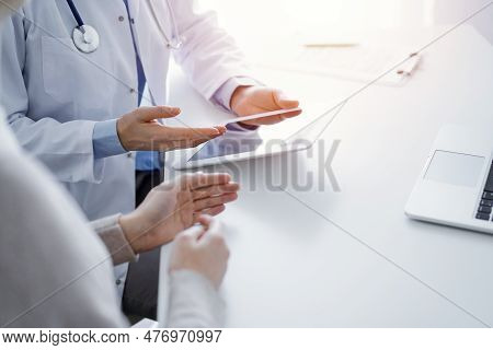 Doctor And Patient Sitting At The Table In Clinic. The Focus Is On Female Physicians Hands Using Tab
