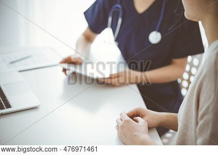 Doctor And Patient Sitting At The Table In Clinic While Discussing Something And Using Tablet Comput