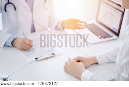 Doctor And Patient Using Tablet Computer While Sitting Opposite Each Other At The Desk In Clinic. Th