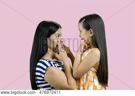 Side View Of Woman And Little Girl Are Making Faces To Each Other. Isolated On Pink Background.