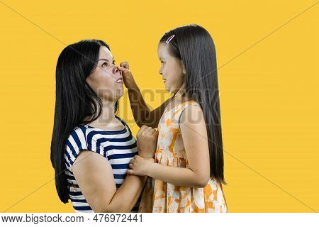 Little Girl Is Making A Piggy Nose To Her Mother. Isolated On Yellow.