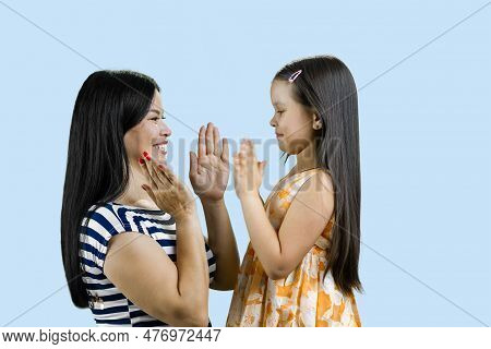 Side View Of Woman And Her Daughter Are Playing Clapping Game. Isolated On Pale Blue.