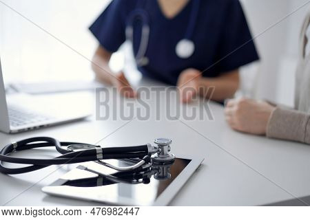 Stethoscope Lying On The Tablet Computer In Front Of A Doctor And Patient At The Background. Medicin