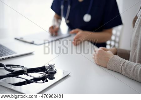 Stethoscope Lying On The Tablet Computer In Front Of A Doctor And Patient At The Background. Medicin