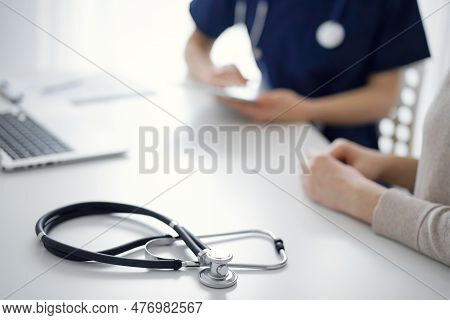 Stethoscope Lying On The Tablet Computer In Front Of A Doctor And Patient At The Background. Medicin
