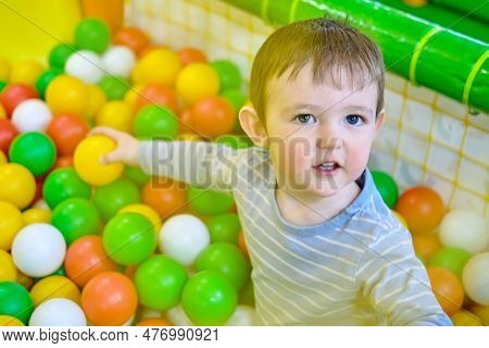 Toddler Baby Plays In The Pool With Balls. Child Boy Crawling In The Pool With Plastic Balls. Kid Ag