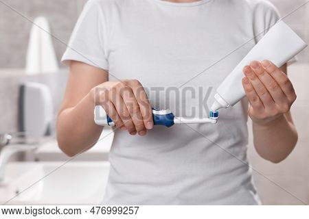 Woman Squeezing Toothpaste From Tube Onto Electric Toothbrush In Bathroom, Closeup