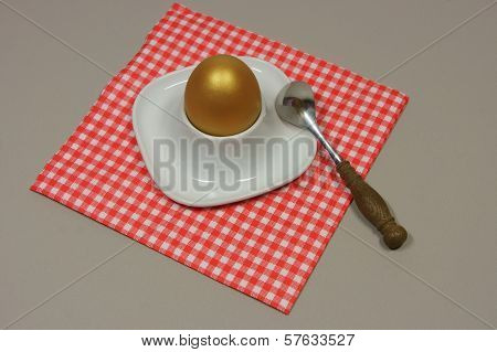 Golden Egg In An Egg Cup On A Red Patterned Napkin With Spoon